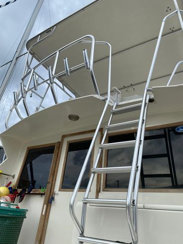 Metal ladder leading to the upper deck of a boat under a cloudy sky.