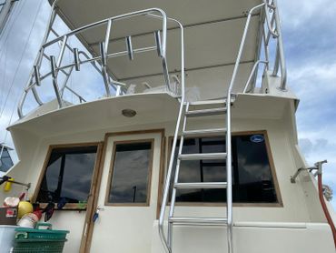 A ladder leading to the upper deck of a boat with windows and a door below.