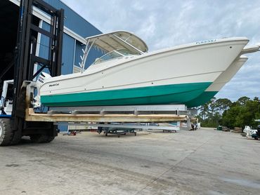 A boat being lifted by a forklift on a concrete surface under a cloudy sky.