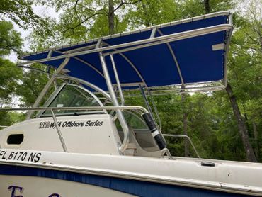 A boat with a blue canopy docked near lush green trees.